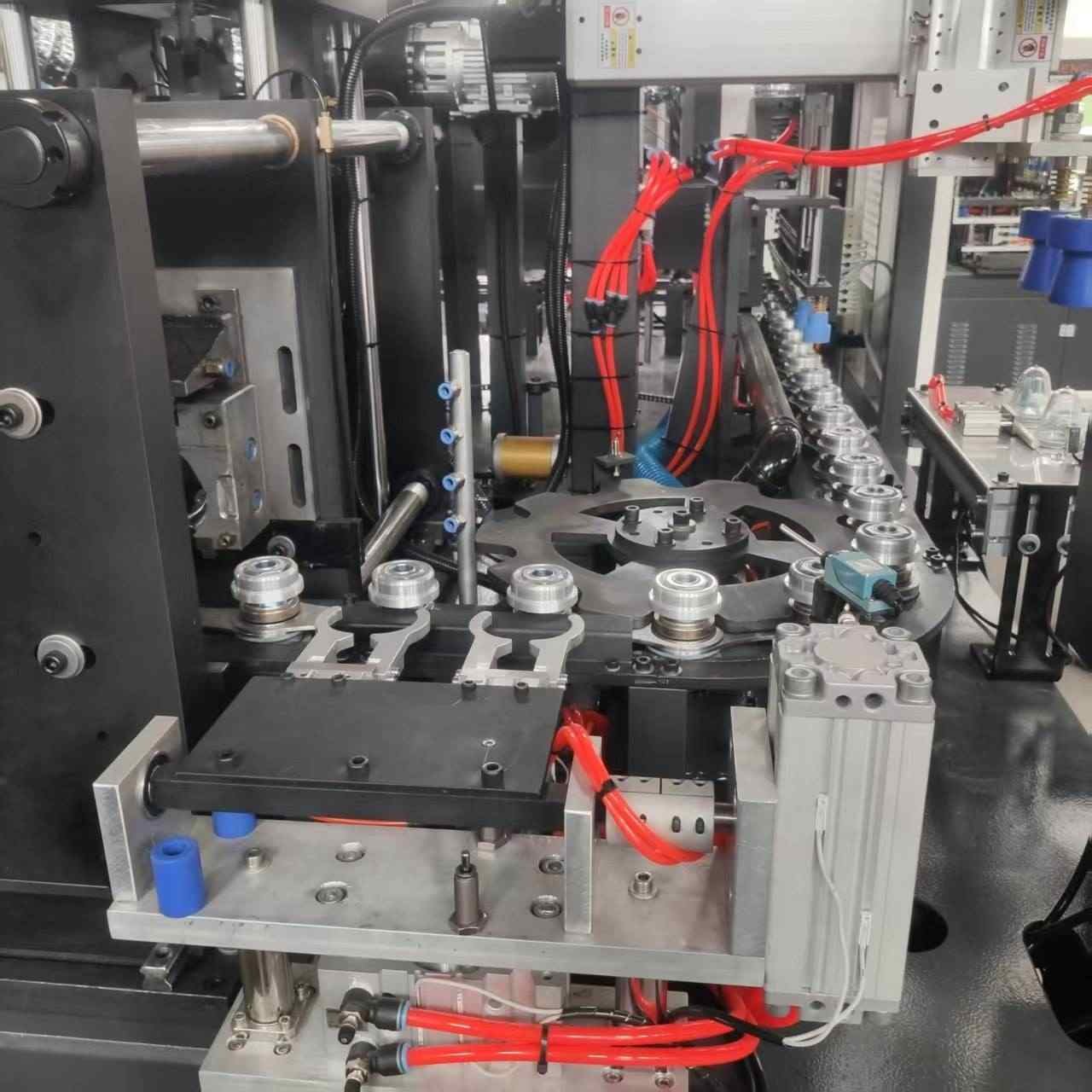 Detail view of automatic preform gripper mechanism and multi-axis transfer arm system in PET stretch blow molding machine — Sailwin